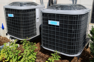 Two HVAc units outside of building, next to green plants.